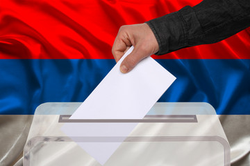 male voter drops a ballot in a transparent ballot box on the background of the national flag of Serbia, concept of state elections, referendum