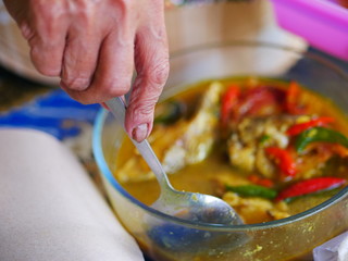 The woman`s hand scoops up a spoon from a bowl of fish soup.