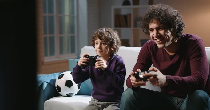 Cute authentic asian brothers with curled hair enjoying their together time, playing football video games in front of tv, parent and son relaxing with their hobby 4k footage