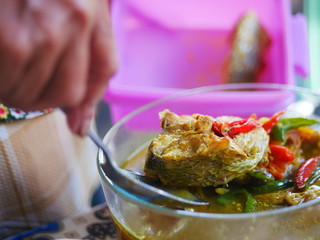 The woman`s hand scoops up a spoon from a bowl of fish soup.