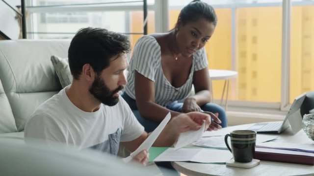 Multiethnic couple filing tax return, preparing home budget. African American woman and Caucasian man checking utility bill and banking account. Married people preparing taxes and form