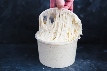 levain full grown in a plastic container with a hand pulling
