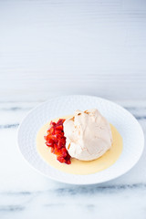 Dessert with meringue, macerated strawberries and creme anglaise on a white plate and white surface