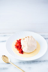 Dessert with meringue, macerated strawberries and creme anglaise on a white plate and white surface