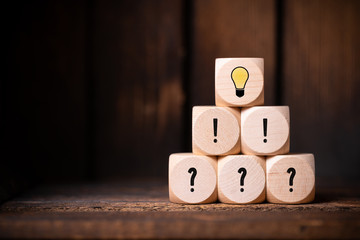 cubes with question marks, exclamation marks and a lightbulb symbol in front of wooden background