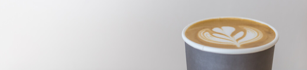 Closup of takeaway paper cup of hot coffee latte with milk foam art use for cover page concept.