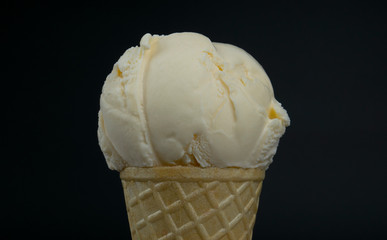 Ice cream flavor Vanilla scoop in waffle cone on black background, Front view Food concept.