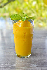 Healthy Mango smoothie frappe in a glass on  wood table in garden background.