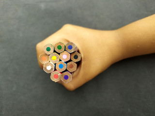 some colorful wooden pencil hold in a child hand on black background