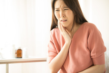 Naklejka premium Woman is sitting on bed in her home, she has toothache. concepts of health and medical care