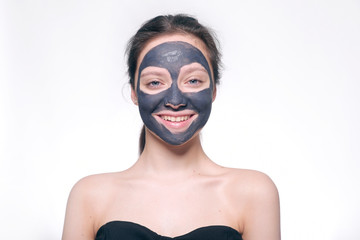 Teenager girl in a black mask, natural photo of a real mask on a young girl. Texture dark cream. Model on a white background smokes skin