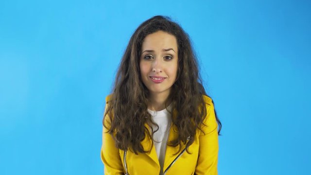 Confused young woman in yellow jacket in Studio with blue Background.