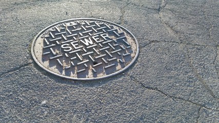 Metal sewer cap on a dry, cracking road during summer
