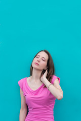 Young woman in front of teal blue wall wearing a bright pink dress and makeup