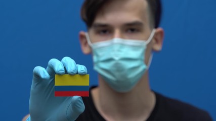 COVID-19 pandemic in Colombia. A young, attractive Colombian man, Latin American in protective medical mask and gloves. The guy is holding the flag of Colombia. Coronavirus pandemic in South America - Powered by Adobe
