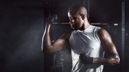 sport portrait of african american athletics strong bodybuilder man posing show his muscle in gym in dark tone