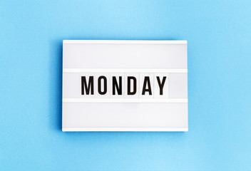Text "monday" on lightbox for holiday - Thank God It’s Monday. Start of working week concept. Top view on blue background.