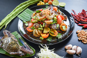 Spicy seafood salad with shrimp crab cockles served on black plate with fresh vegetables herbs and spices - Menu Thai Food