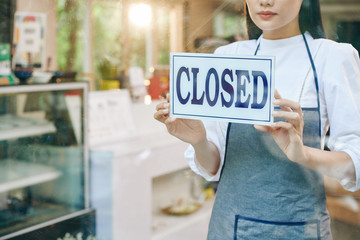 Sad female restaurant owner closing door and hanging sign