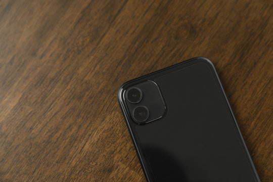 The back of black smartphone on the wood table.