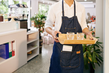 Cropped image of waiter carrying wooden tray with glasses of fresh cold water