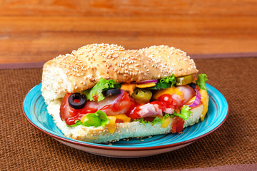 Sandwich with meat, cheese and fresh vegetables, closed, on wooden background