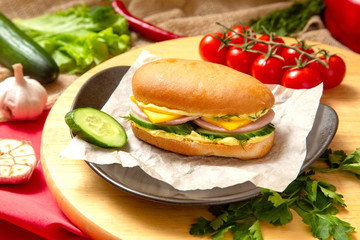 Sandwich with meat, cheese and fresh vegetables, closed, on wooden background