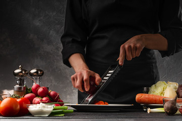 Chef rubs beets for cooking. Against the background of vegetables and ingredients. Cooking tasty and wholesome food. Restaurant business, recipe book.