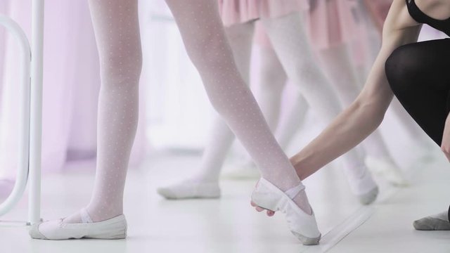 Close up feet of unrecognizable little girls in white socks and ballet shoes, their ballet teacher correcting them