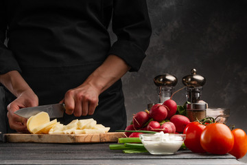The chef cuts potatoes for cooking potatoes in French. Against the background of vegetables. With space for advertising, restaurant business, and cooking. Book of recipes