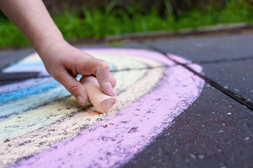 Closeup of child hand drawing rainbow using colorful chalk