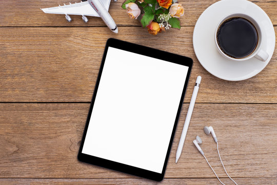 Mockup image of black tablet computer with blank white screen, airplane and cup of coffee isolated on wood table background. Business transportation, trip and travel concept. Flat lay. Top view.