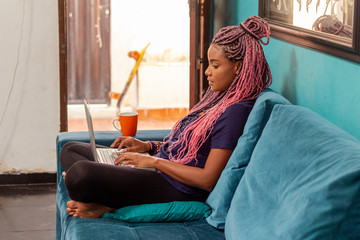 Obraz premium Young black woman with braid using notebook in home room