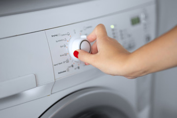 The girl sets the washing program for the washing machine.