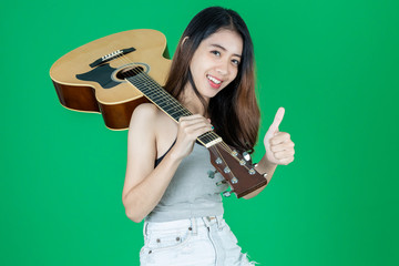 Attractive young Asian lady with acoustic guitar over green isolated background.
