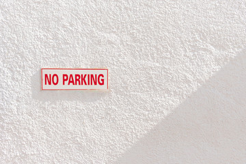 Close up No parking sign at white concrete wall with shade and shadow. Copy space for text.