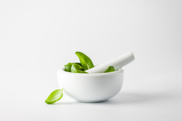 Basil leaves in a mortar on a white background - obrazy, fototapety, plakaty