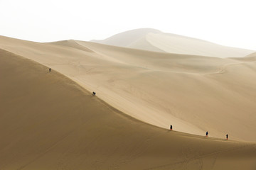 Fototapeta na wymiar Tourists climbing the sand mountain or the singing sand dunes at Mingsha Shan desert as part of the Silk Road, Dunhuang, Gansu, China.