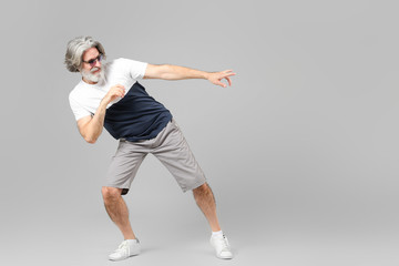 Cool senior man dancing against grey background
