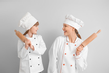 Portrait of female chef and her little daughter on light background