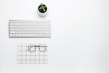 Computer keyboard with notebook and eyeglasses on white background
