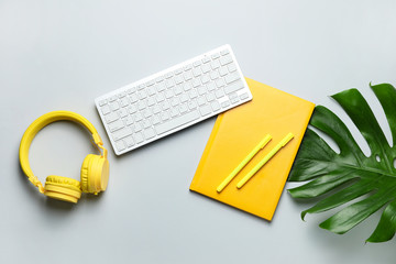 Computer keyboard with notebook, headphones and pens on light background
