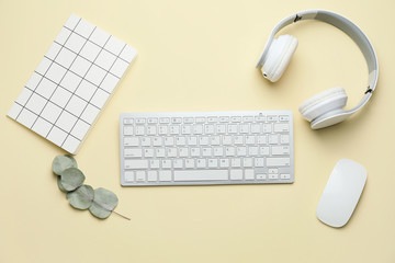 Computer keyboard with notebook and headphones on color background