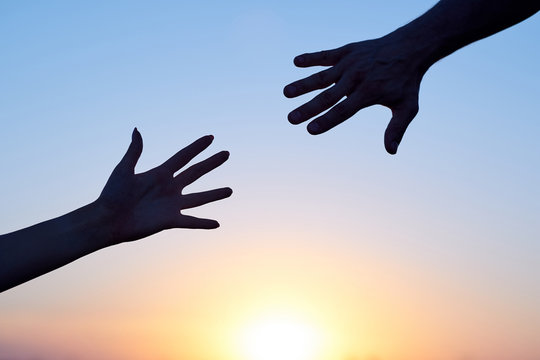 Giving a helping hand. Silhouette Two hands, man and woman, reaching towards each other at sky sunset