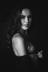 Closeup portrait of a brown-eyed brunette woman of 32 years with beautiful healthy hair in lace underwear on a black background. Soft selective focus. Black and white art photography.