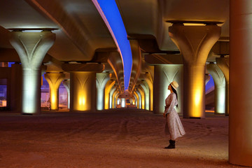 Woman standing under traditional modern automotive bridge with lights layers background, Bahrain.