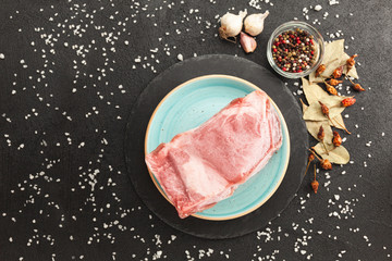 Frozen piece of raw meat on plate on black table. Rime on product, thawing.