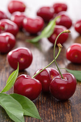 Sweet red cherry berries with green leaves on  wooden background. Studio shot, copy space.
