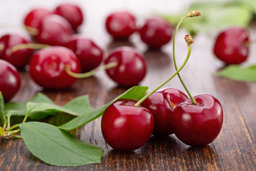 Red, juicy cherries with leaves, close-up on  brown wooden background. Studio shot, copy space.