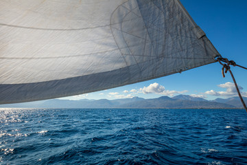 Sail boat with set up sails gliding in open sea near islands